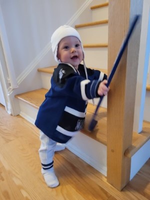 Jeff wears a Toronto Maple Leafs jersey and holds a hockey stick, standing in front of a staircase.